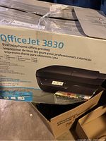 Box of HP OfficeJet 3830 shows branding and printer model on packaging, slightly damaged box visible.