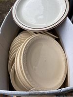 Top view of a box with stacked beige Syracuse restaurant ware plates with a decorative embossed rim pattern