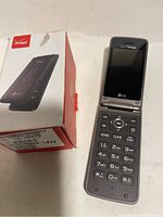 LG flip phone open showing keypad and screen with Verizon logo, next to original box