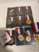 Nine vintage sports medals with red, white, blue ribbons, some in plastic cases.