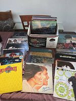 Wide shot of box and table with vinyl records laid out and stacked, showing a variety of titles and artwork styles