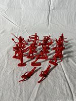 Overhead angled view of all red plastic Olympic action figures arranged together on white backdrop showing multiple sports figures in standing poses, some with bases, two figures have detached bases shown near front.