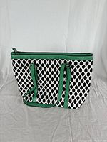 Front and side view of Bueno shoulder bag showing black geometric pattern on white fabric with green leather trim and handles.