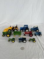 Top view of all toy tractors and small trailer arranged on white fabric with a coin for scale