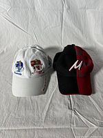 Two baseball caps on a white background, one white with Disney princess embroidery and one black and red with Mickey Mouse design.