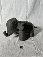 Front angled view of the grey faux leather elephant door stopper with a coin for size reference.