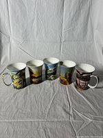 Five Group of Seven collectible mugs arranged in a row side view, showing full mug designs and handles.
