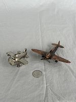 Miniature silver airplane pencil sharpener and bronze-colored airplane model next to a quarter for size reference.