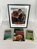 Full view of framed Goldfinger poster with three books beneath it, showing lot contents clearly.