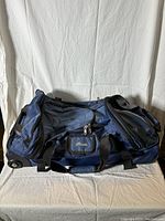 Side view of the blue Roots travel luggage bag lying flat to show side pockets, wheels, handles, and overall condition.