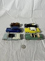 Front view of six toy diecast cars arranged in two rows with a quarter coin for scale, showing car details and colors.