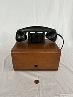 Front view of vintage Dictograph telephone intercom substation phone showing wooden box and black handset resting on top, penny for scale.
