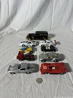 Ten diecast toy cars displayed on white cloth with visible wear and a coin for scale.