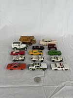 Overview of all 15 vintage diecast toy vehicles arranged on white fabric background with quarter coin for scale.