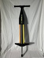 Full view of vintage pogo stick showing T-shaped handle, large central spring, orange and yellow side bars, and textured footrests
