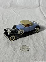 Front angle view of the diecast model car with blue body, cream top, showing missing engine cover and chrome details.