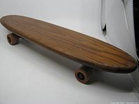 Side view of vintage wooden skateboard showing wood grain deck and clay wheels.