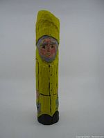 Front view of the carved wood fisherman painted in yellow raincoat and hat, holding bait bucket