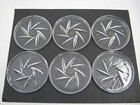 Top view of six round glass crystal drink coasters on dark background, showing etched leaf/star pattern.