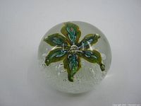 Front angle of glass paperweight showing green and blue floral design with bubbles inside.