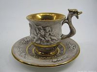 Front angle of the R. Capodimonte teacup and saucer showing cherub relief on cup and ornate saucer design with gold accents.