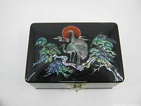 Top view of black lacquered jewelry music box showing crane and pine tree design with red sun in mother-of-pearl inlay.