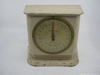 Front view of old Justa-Arista scale showing rectangular shape, beige paint with wear, and circular dial with brass bezel.