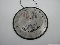 Close-up photo of the metal bar compass showing cocktail names, ingredient abbreviations, and instructions.