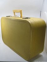 Front side of yellow vintage suitcase luggage showing textured surface, handle and metal clasps.