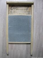 Front view of wooden washboard with corrugated metal scrubbing surface and manufacturer's label.