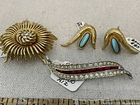 Lot display showing all three pieces: round brooch with clear stones, matching earrings with turquoise stones, and a long brooch with clear and red stones.