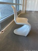 Side view showing the chair's curved cantilever base and overall shape, highlighting its white molded plastic construction and some scuffs.
