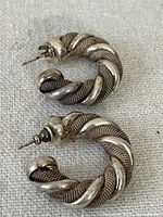 Pair of sterling silver twisted design hoop earrings with post backs, displayed on a light fabric surface.
