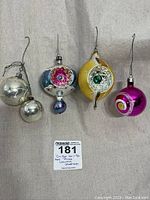 Photo showing all five vintage 1950s Christmas ornaments with various shapes and colors on a light fabric background.
