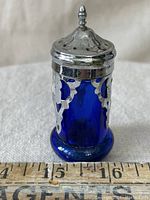 Front view of cobalt blue pepper shaker with metal threaded top and ruler showing size approx 3 inches tall.