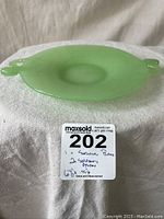 Top-down view showing the oval shape and surface of the green jadite plate with fish serpent handles on each side.