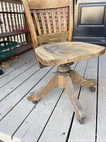 Front-side view of vintage kids oak school chair showing slatted back, wooden seat, and four-legged base with casters on a wooden deck.