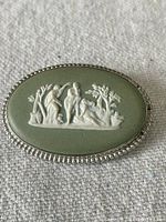 Front view of the oval Wedgwood green jasperware cameo brooch with white classical figure relief and sterling silver beaded border.