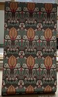 Full length view of C.F.A. Voysey The Owl wallpaper roll laid out showing repeated owls and floral pattern in red and olive tones.
