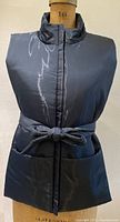 Front view of the navy blue shiny vest, showing the high collar, belt tied at waist, and two front pockets.