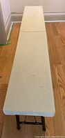 Full length view of rectangular folding bench with off-white plastic top.
