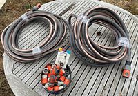 Two coiled brown Gardena garden hoses with orange and black fittings on an outdoor wooden table.