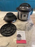 Photo showing the Instant Pot base unit, air fryer lid, base ring, metal cooking rack, and user manual arranged on countertop.