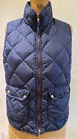 Front view of navy quilted down vest on mannequin, showing diamond quilting, front zipper, high collar, and flap pockets with brass snaps.