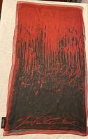 Full length view of the sheer silk scarf showing the red and black abstract print and Jean Paul Gaultier signature at the bottom edge.