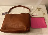 Lot showing both brown leather handbag with braided strap and pink vinyl evening bag with chain strap