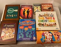Photo showing all 8 games in the lot including Scrabble, Clue, Codenames, Debatable, Chess, This That & Everything, Balderdash, and Jenga boxed games arranged on a surface.
