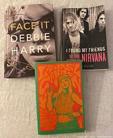 Three music books laid out on fabric background showing covers of 'Face It Debbie Harry', 'I Found My Friends Nirvana', and colorful 'Laurel Canyon' book.