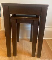 Front view of larger and smaller nesting dark brown wood tables stacked together