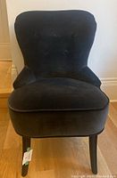 Front view of a dark brown upholstered occasional chair with button tufting and wooden legs on a wood floor.